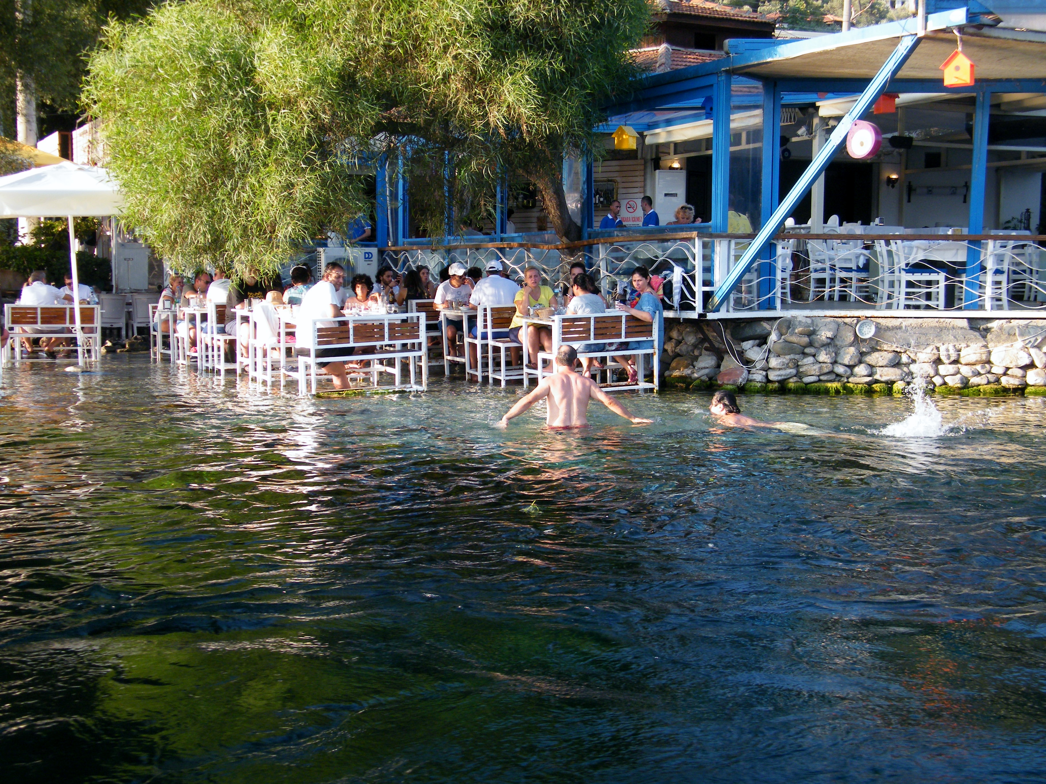 Gente que se baña entre las mesas de un restaurantes posadas en la orilla del río de Akyaka en el Egeo turco / J.M Akyaka en el Egeo turco 